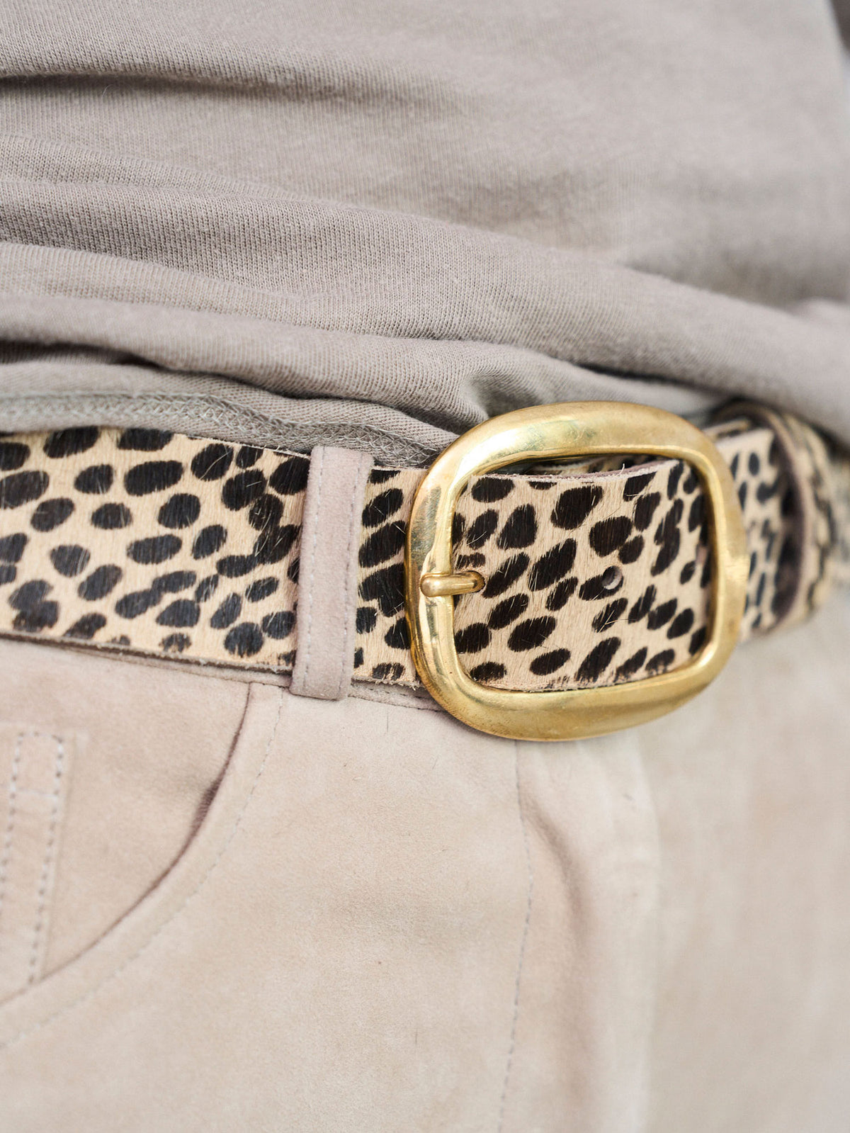 A close-up of a leopard print belt with a gold buckle, worn with a gray top and beige pants.