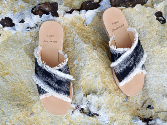 Pair of black and white sandals with frayed edges on a textured surface