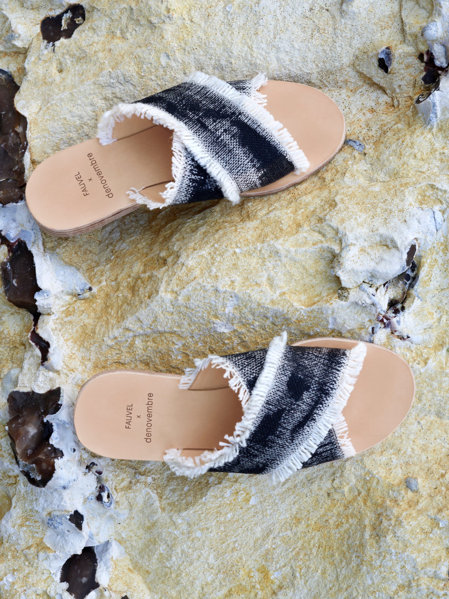 Pair of black and white sandals with frayed edges on a textured surface