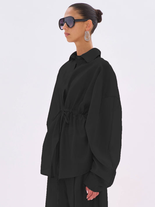 Person wearing a black outfit with sunglasses and earrings on a white background