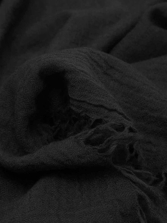 A close-up of dark charcoal gray or black textured fabric with frayed edges, shown in soft folds.