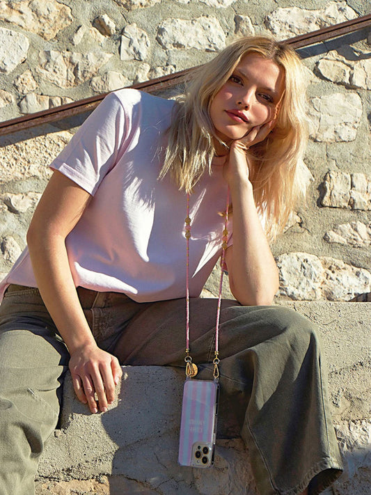 Woman sitting against a stone wall with a phone case hanging from her neck.