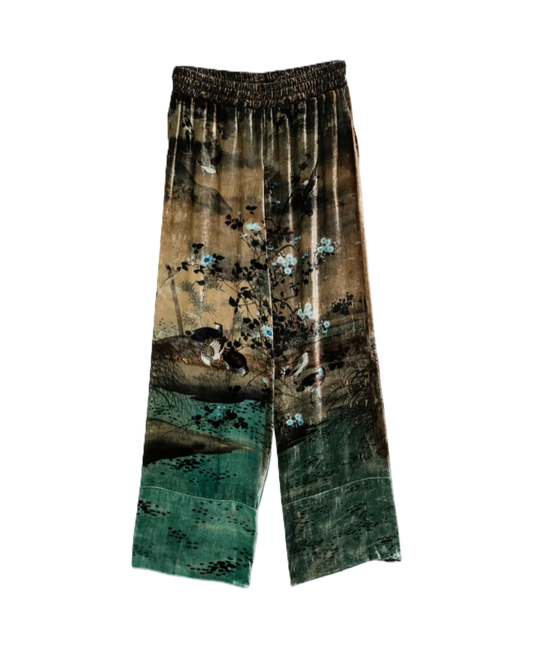A pair of wide-leg cropped pants featuring a vintage-style landscape print with a brown and green color palette, blue blossoms, and birds, finished with an elastic waistband.