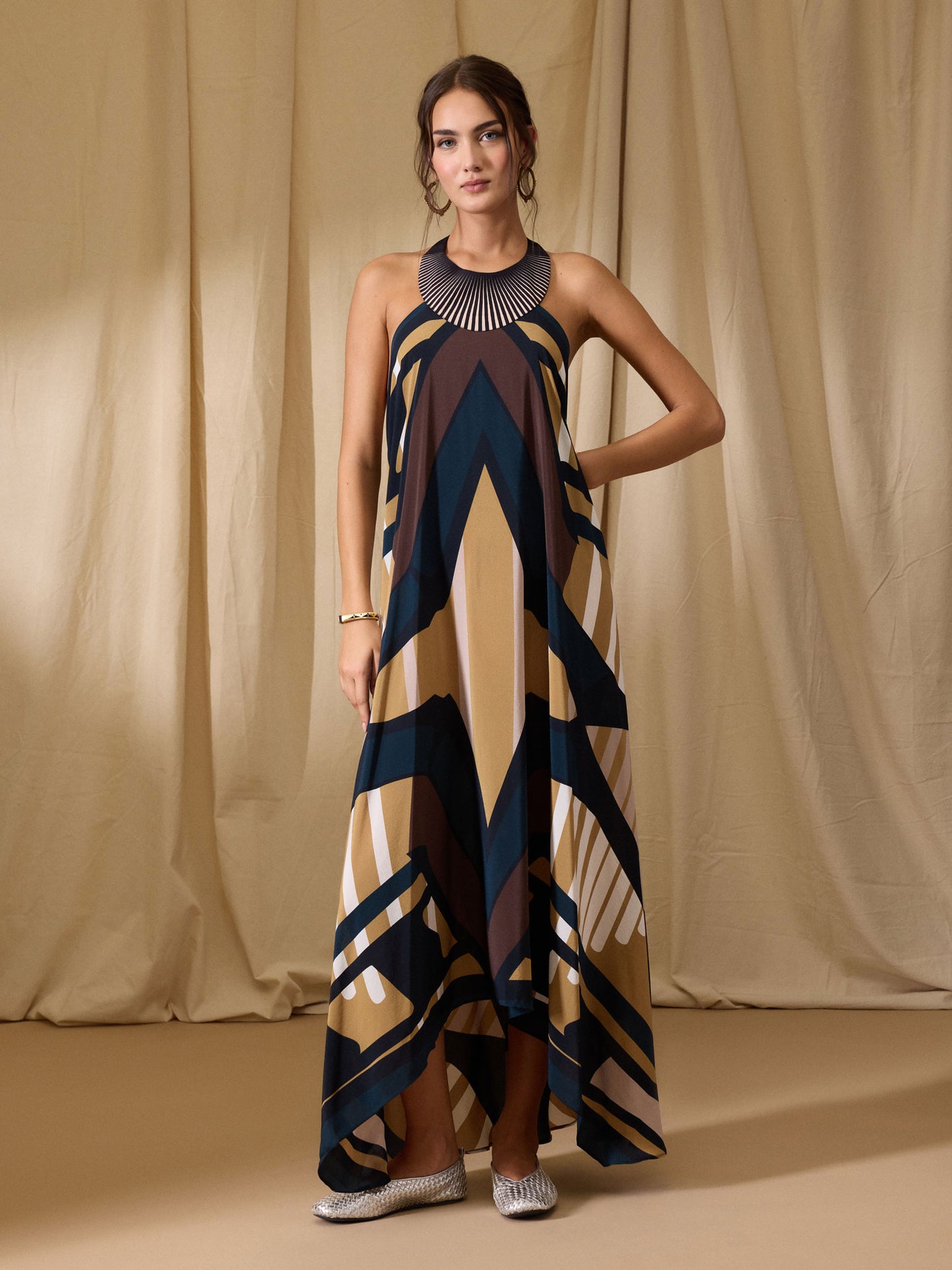 Woman wearing a long, patterned dress against a beige curtain background