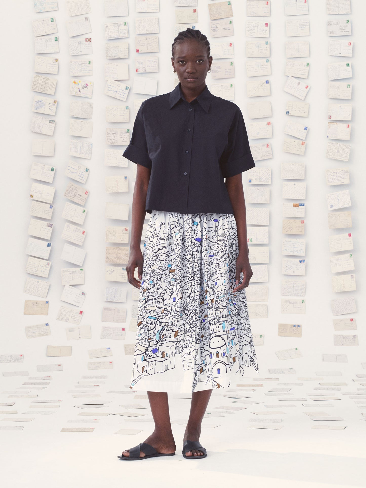Person wearing a black shirt and patterned skirt against a textured wall.