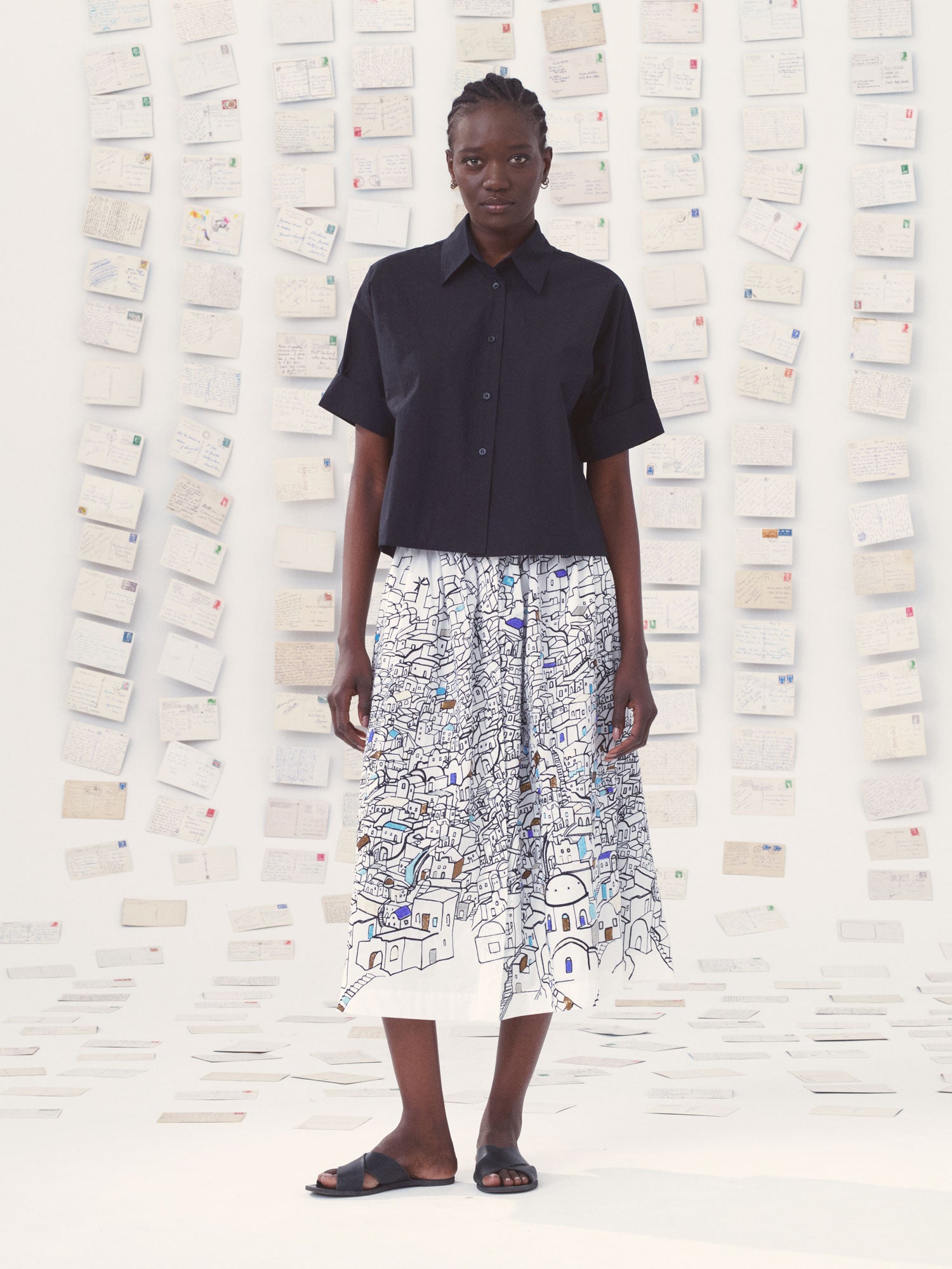 Person wearing a black shirt and patterned skirt against a textured wall.