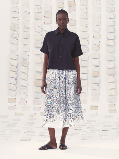 Person wearing a black shirt and patterned skirt against a textured wall.
