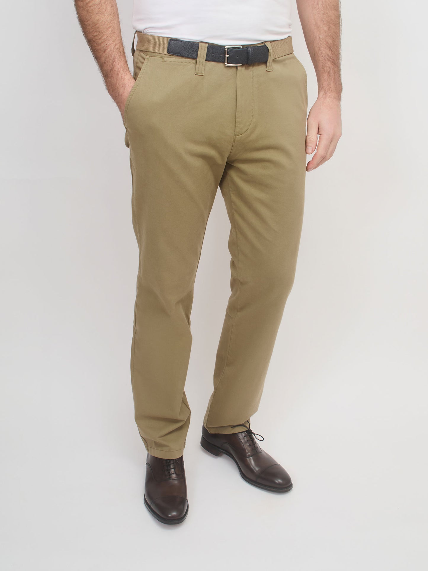 Person wearing beige pants with a white shirt and brown shoes on a light gray background