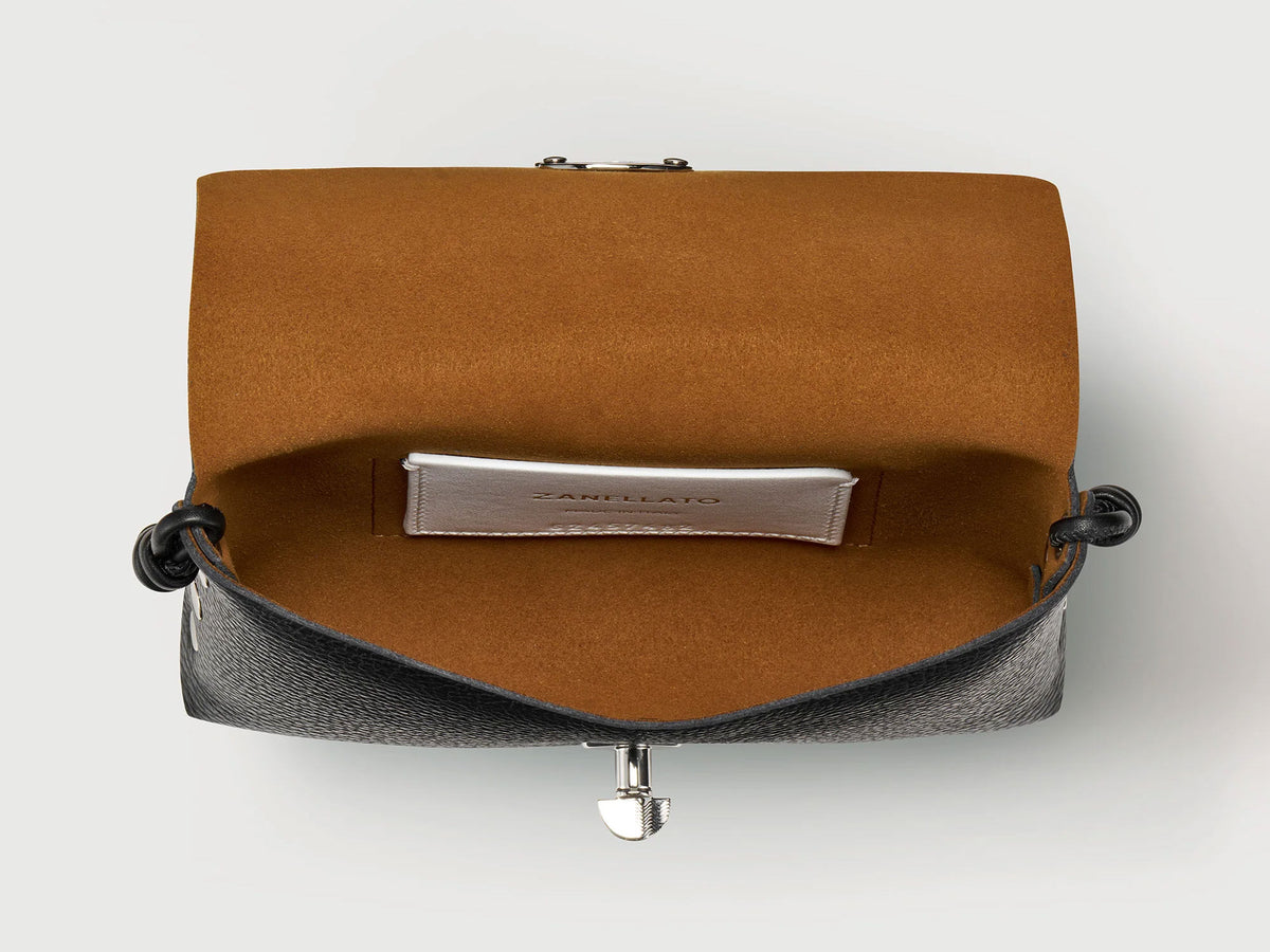 An open black leather clutch bag with a warm brown suede-like interior lining and a silver-tone metal clasp, shown against a light gray background.