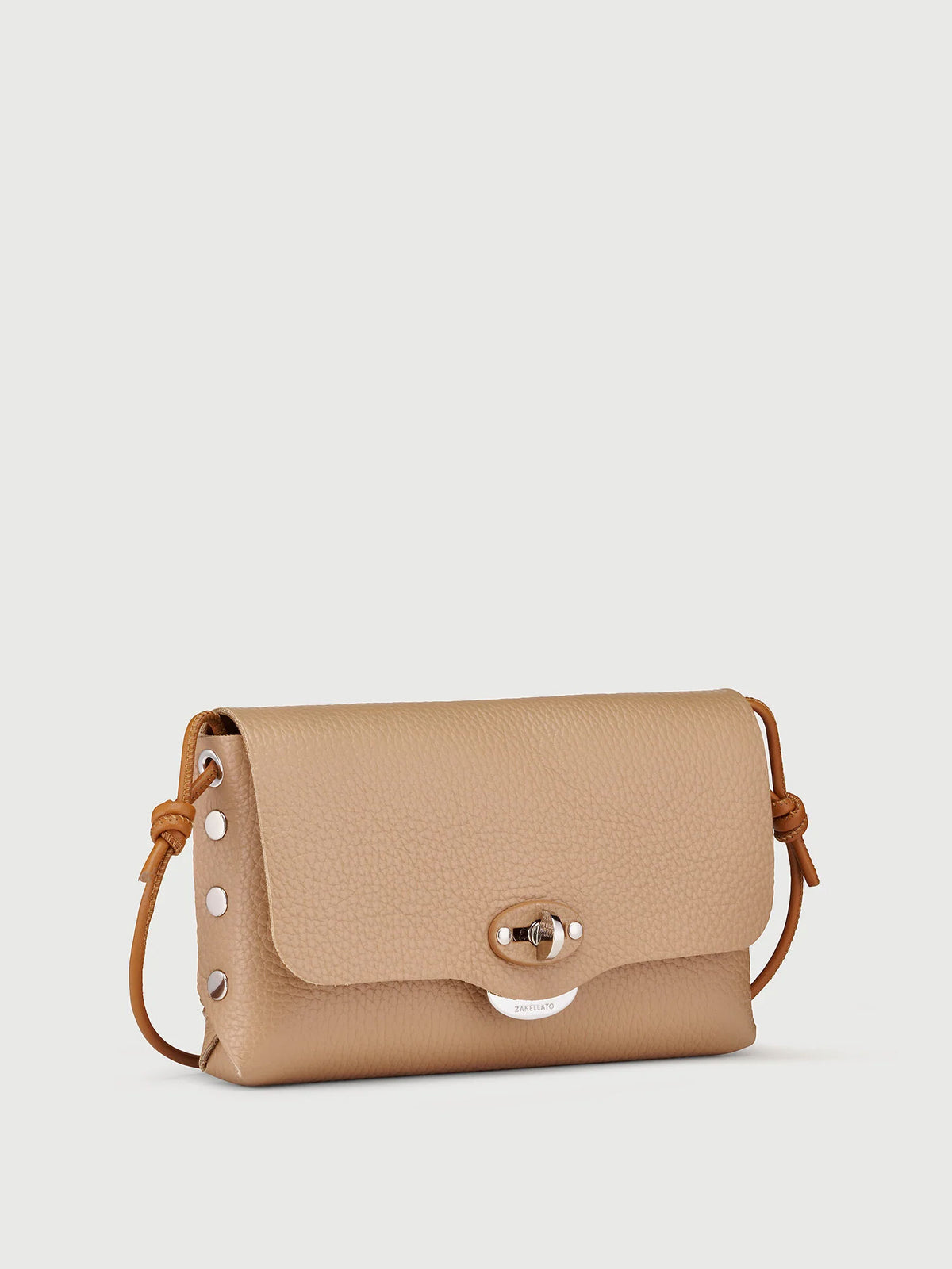 A small tan pebbled leather crossbody bag with a flap closure, silver-tone hardware, and a thin brown leather strap, shown on a light gray background.