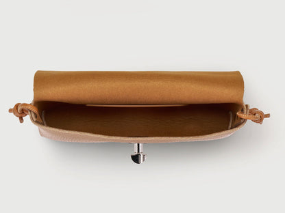 A top-down view of a tan leather clutch bag with a rolled satin gold interior lining and a silver metal snap closure, set against a plain light gray background.