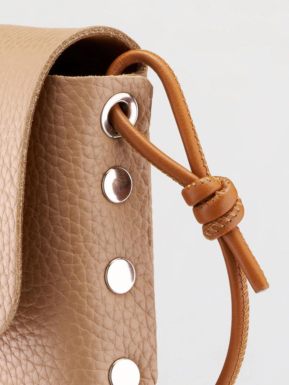Close-up of a tan pebbled leather bag with a matching leather drawstring cord knotted through silver-tone metal grommets.