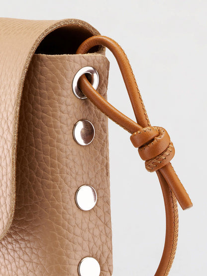 Close-up of a tan pebbled leather bag with a matching leather drawstring cord knotted through silver-tone metal grommets.