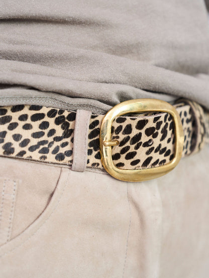 A close-up of a leopard print belt with a gold buckle, worn with a gray top and beige pants.