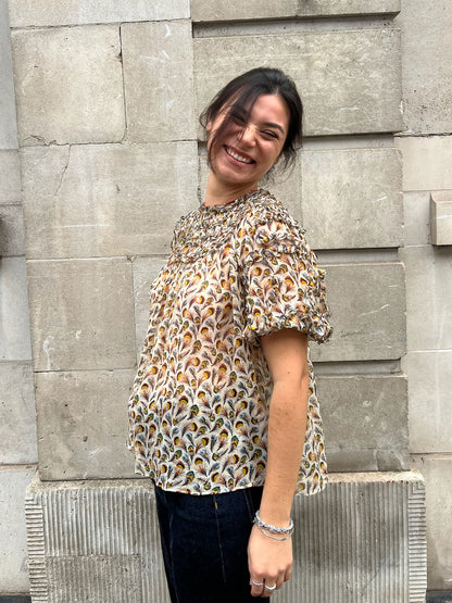 Woman wearing a patterned blouse standing against a stone wall.