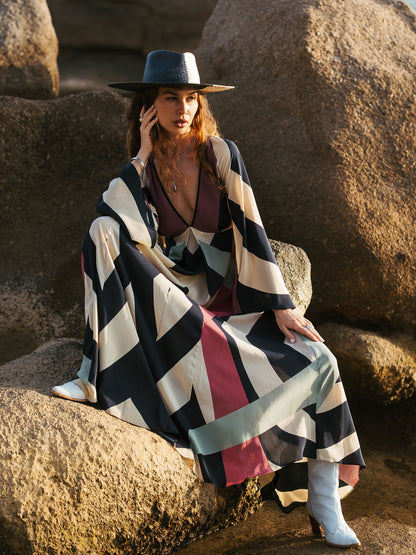 Woman sitting on rocks wearing a colorful striped dress and wide-brimmed hat.