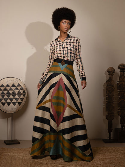 Woman wearing a patterned skirt with a checkered top, standing in a room with decorative items.