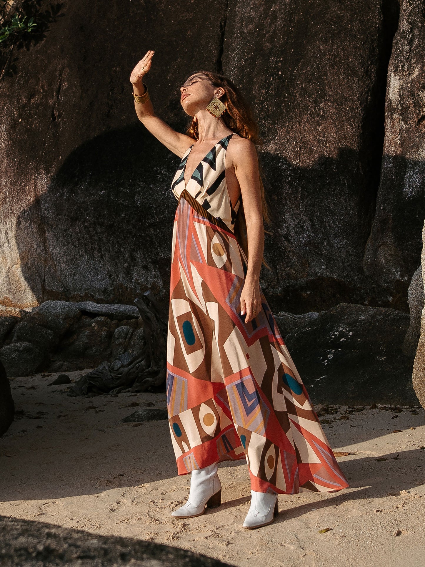 Woman in a colorful dress standing on a beach with large rocks in the background