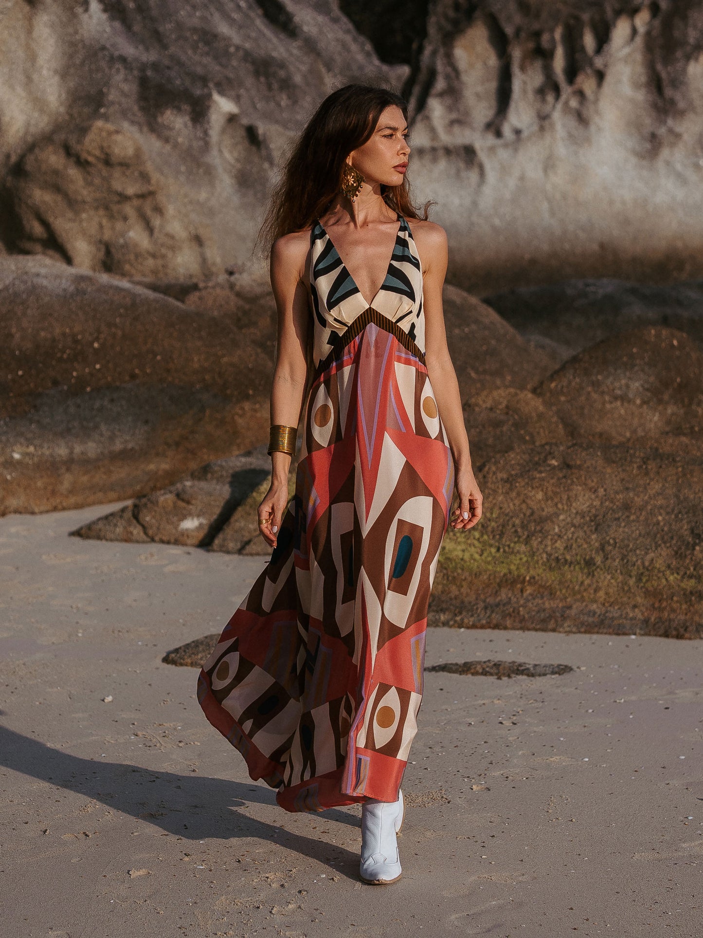 Woman in a patterned dress standing on a beach with rocky background