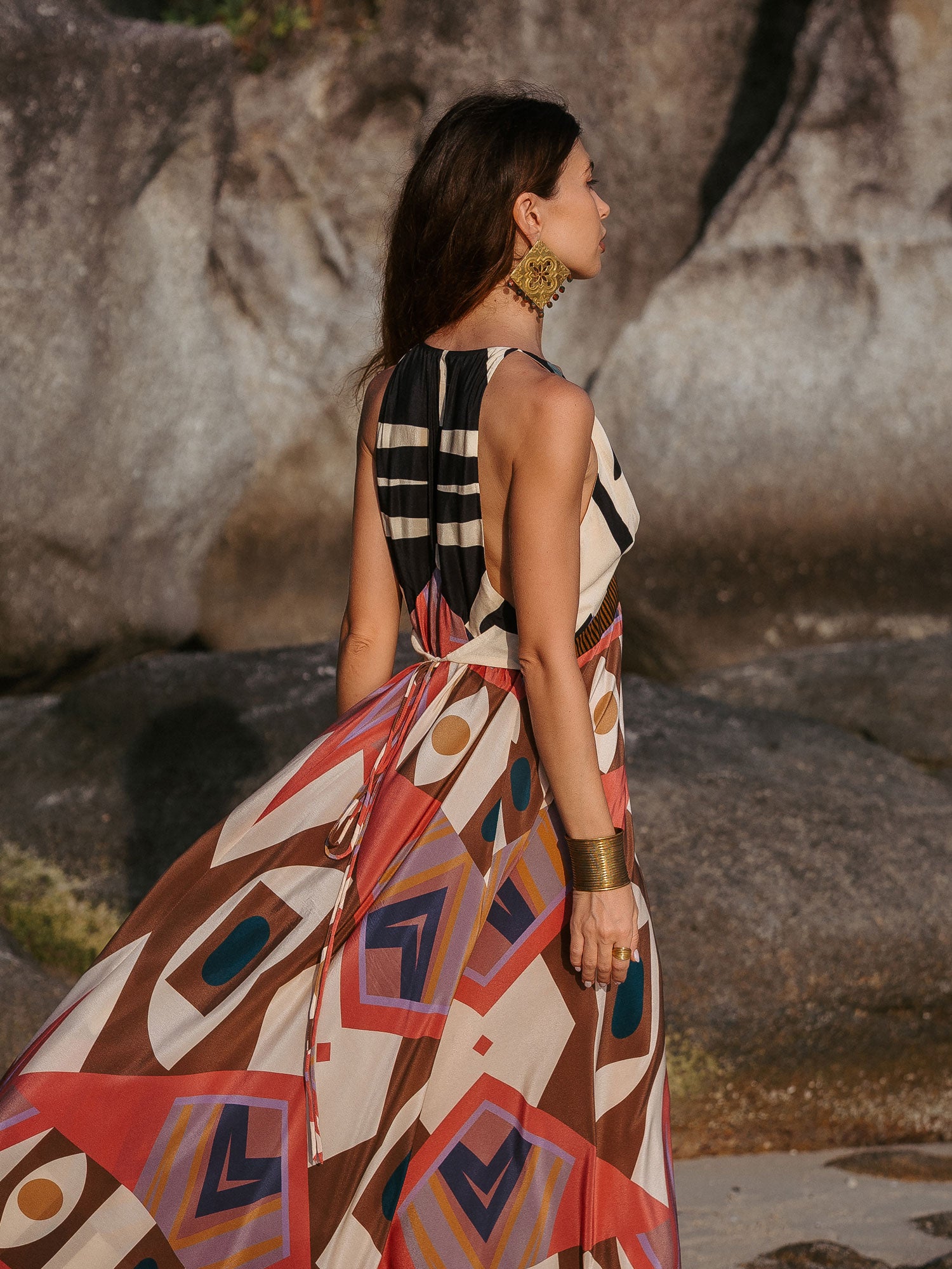 Woman in a patterned dress standing against a rocky background