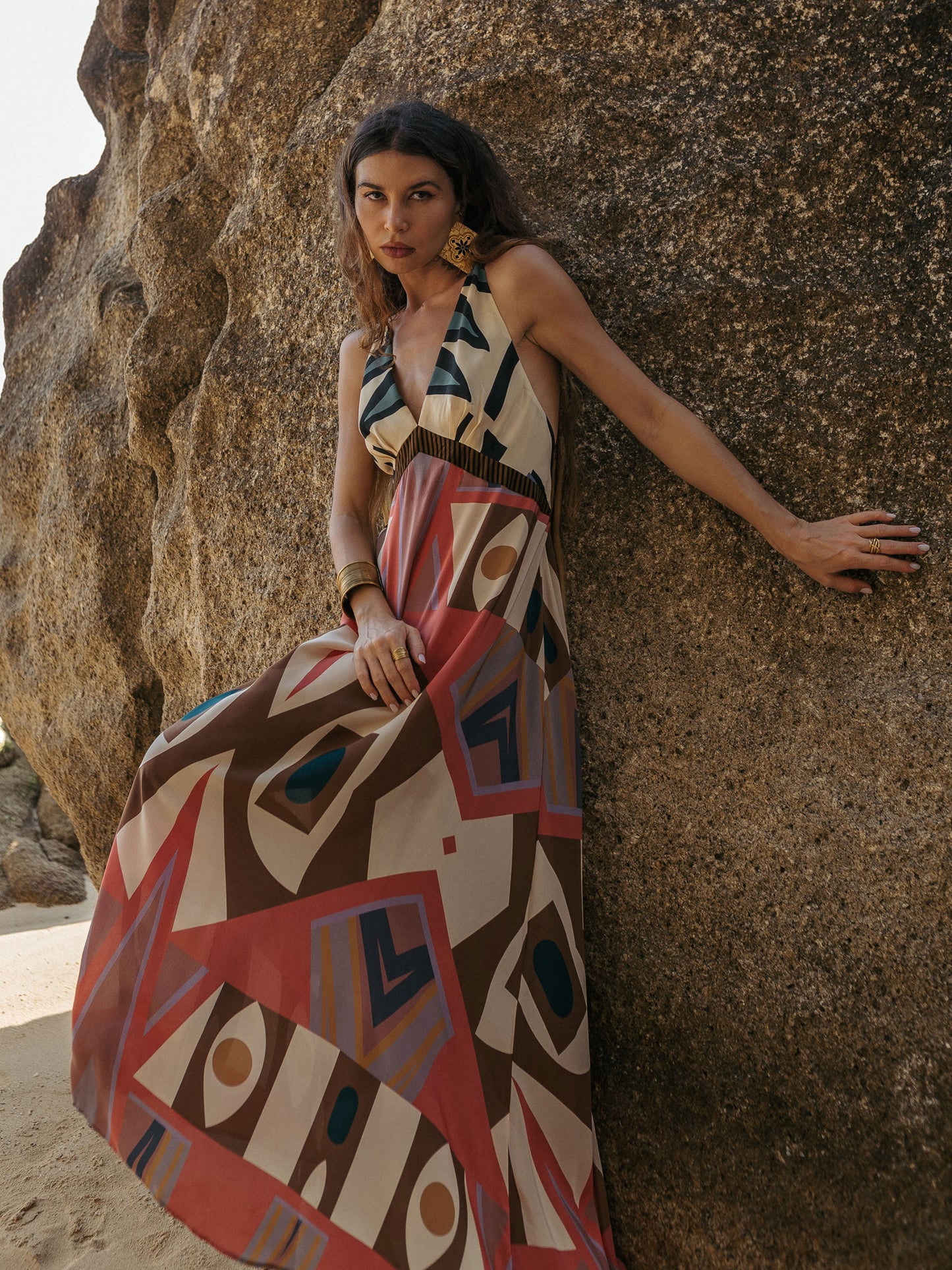 Woman in a patterned dress leaning against a rock wall.