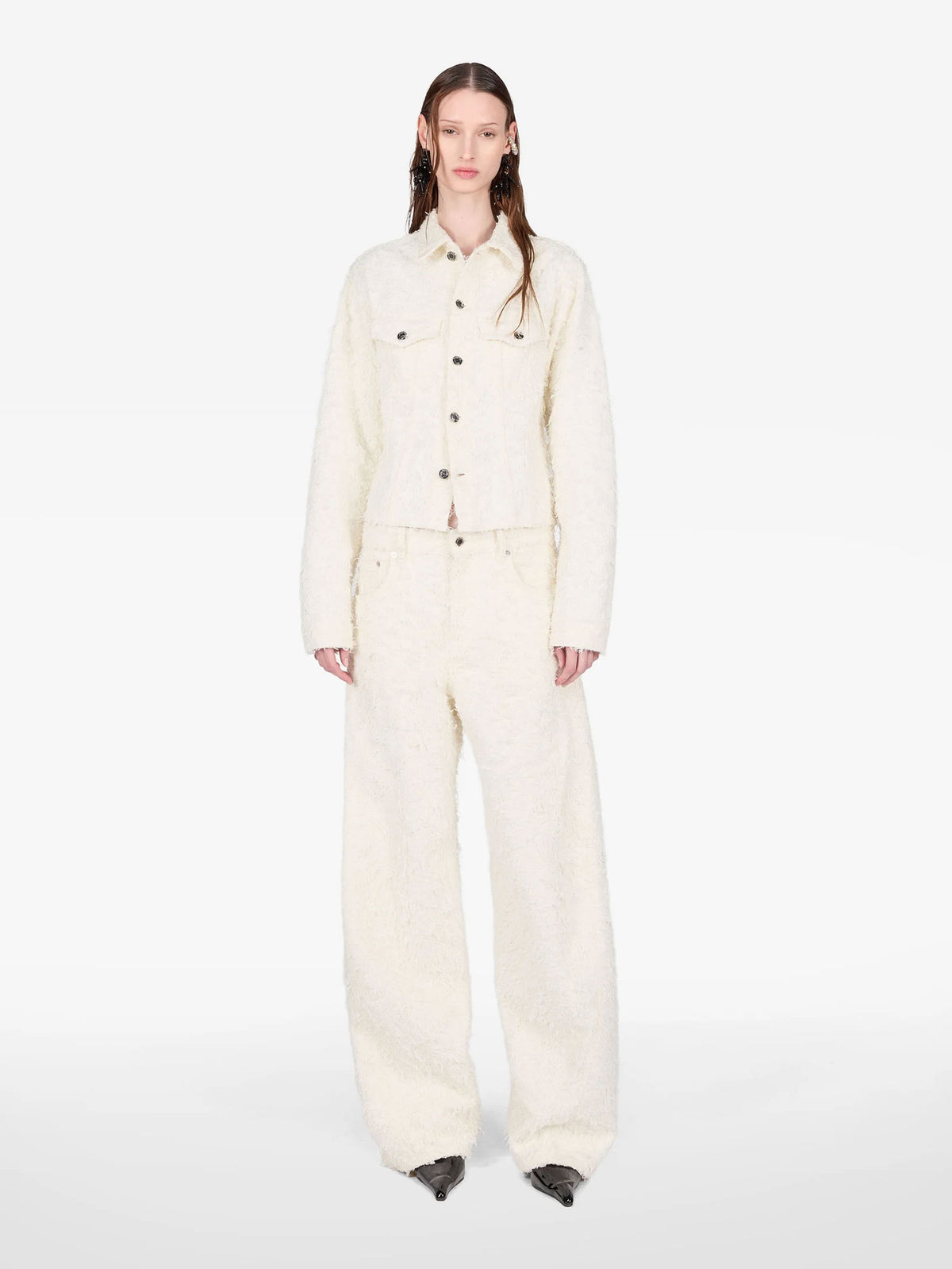 A model stands against a plain white studio background wearing a matching cream-colored textured jacket and wide-leg trousers set.