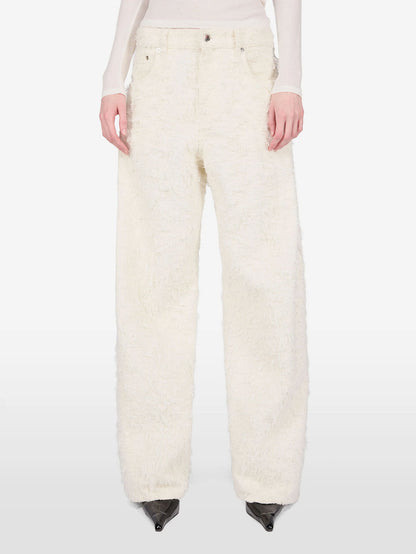 A model is shown from the waist down wearing a pair of wide-leg, high-pile textured cream pants, paired with a light beige long-sleeve top and black pointed-toe heels, against a plain white studio background.