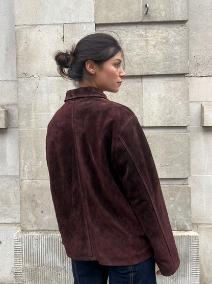 Person wearing a brown jacket standing against a stone wall.
