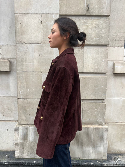 Woman wearing a brown jacket standing against a stone wall.