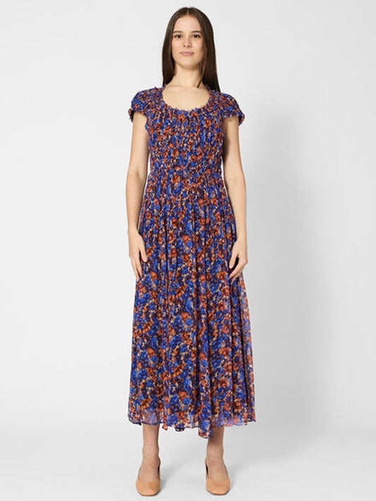 A woman modeling a short-sleeved midi dress with a blue, orange, and red floral pattern against a light gray studio background.