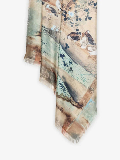 A lightweight rectangular scarf with fringed edges, featuring an artistic print of birds perched on branches over a landscape in muted beige, teal, brown, and blue tones, shown against a plain white background.