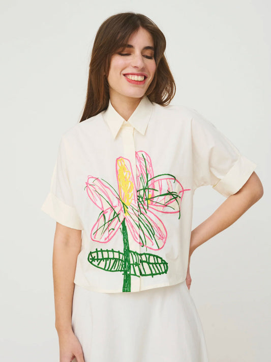 Woman wearing a white Mii shirt with a colorful floral design on a plain background