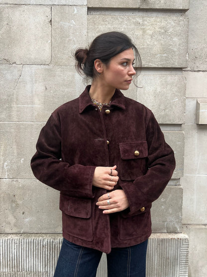Woman wearing a brown suede jacket standing against a stone wall.
