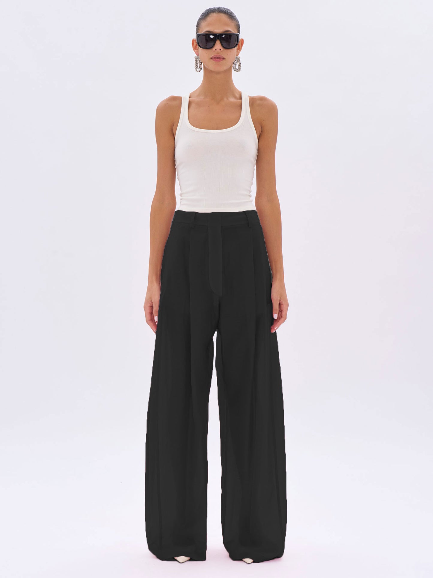 Woman wearing a white tank top and black wide-leg pants on a white background