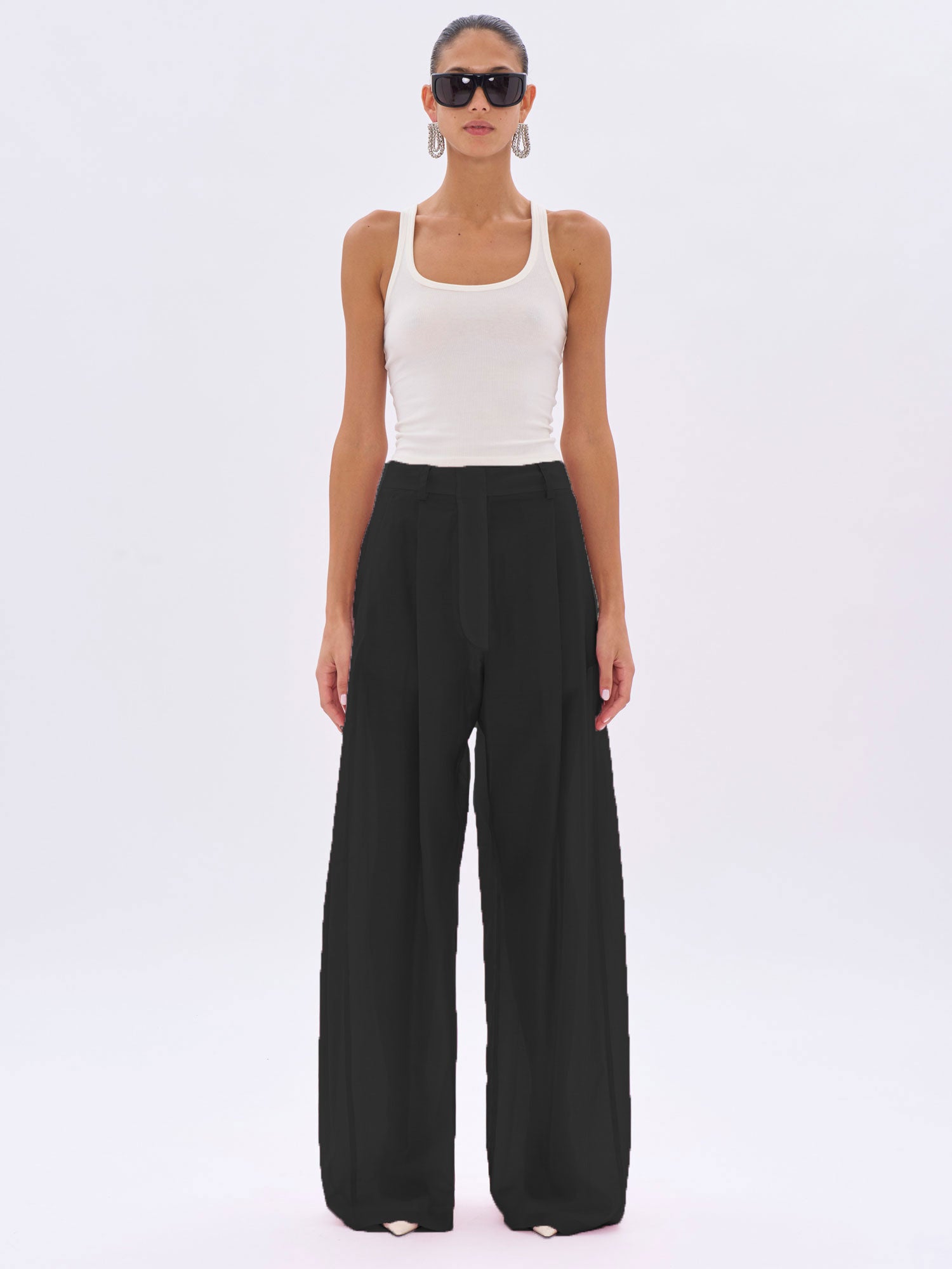 Woman wearing a white tank top and black wide-leg pants on a white background