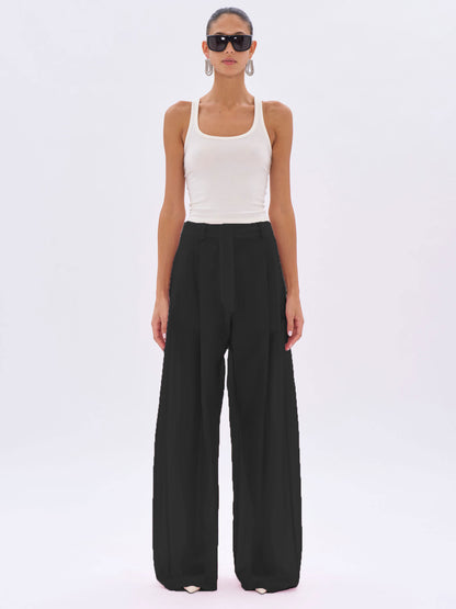Woman wearing a white tank top and black wide-leg pants on a white background