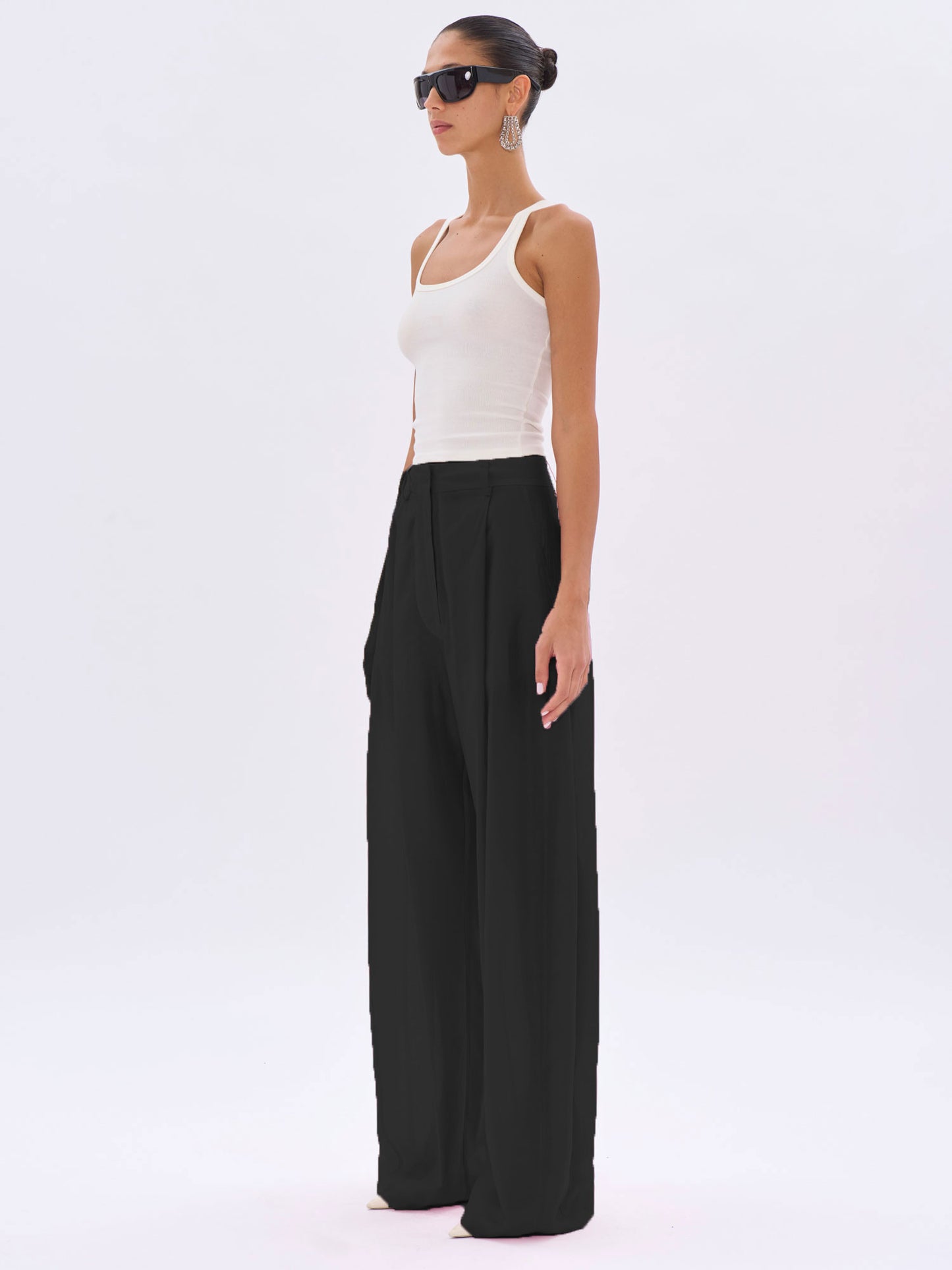 Woman wearing a white tank top and black wide-leg pants on a white background
