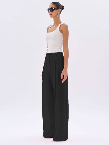 Woman wearing a white tank top and black wide-leg pants on a white background