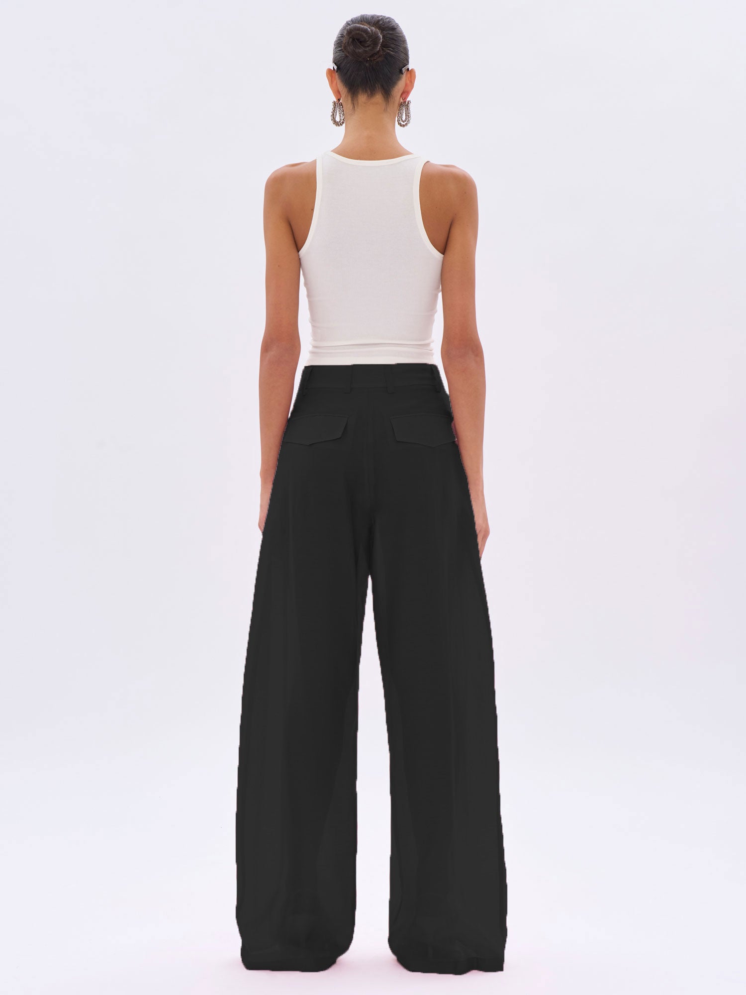 Person wearing a white sleeveless top and black wide-leg pants on a white background