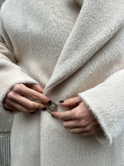 Close-up of hands buttoning a cream coat