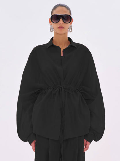 Person wearing a black outfit with wide sleeves on a white background