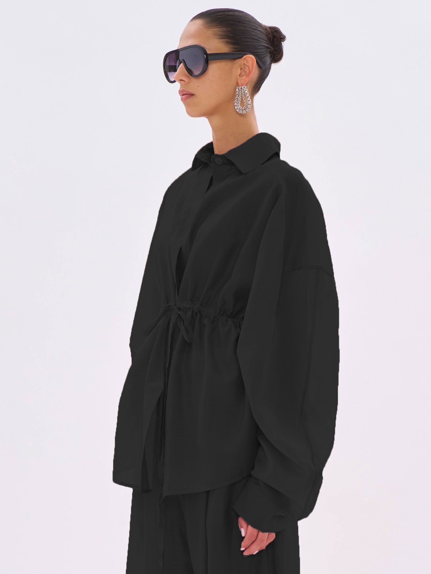 Person wearing a black outfit with sunglasses and earrings on a white background