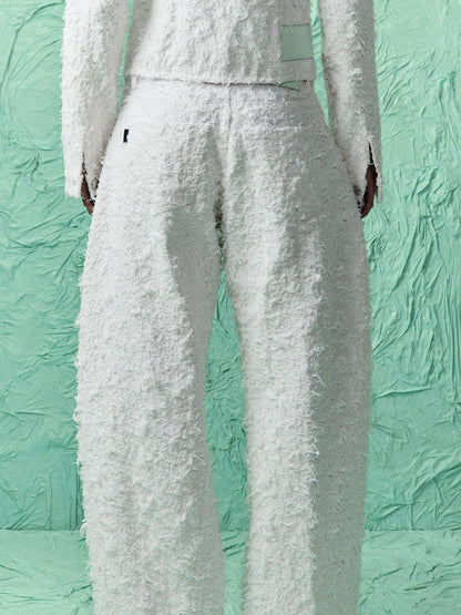 White textured bouclé pants with a matching cropped top, shown from the back on a model against a textured mint green backdrop.
