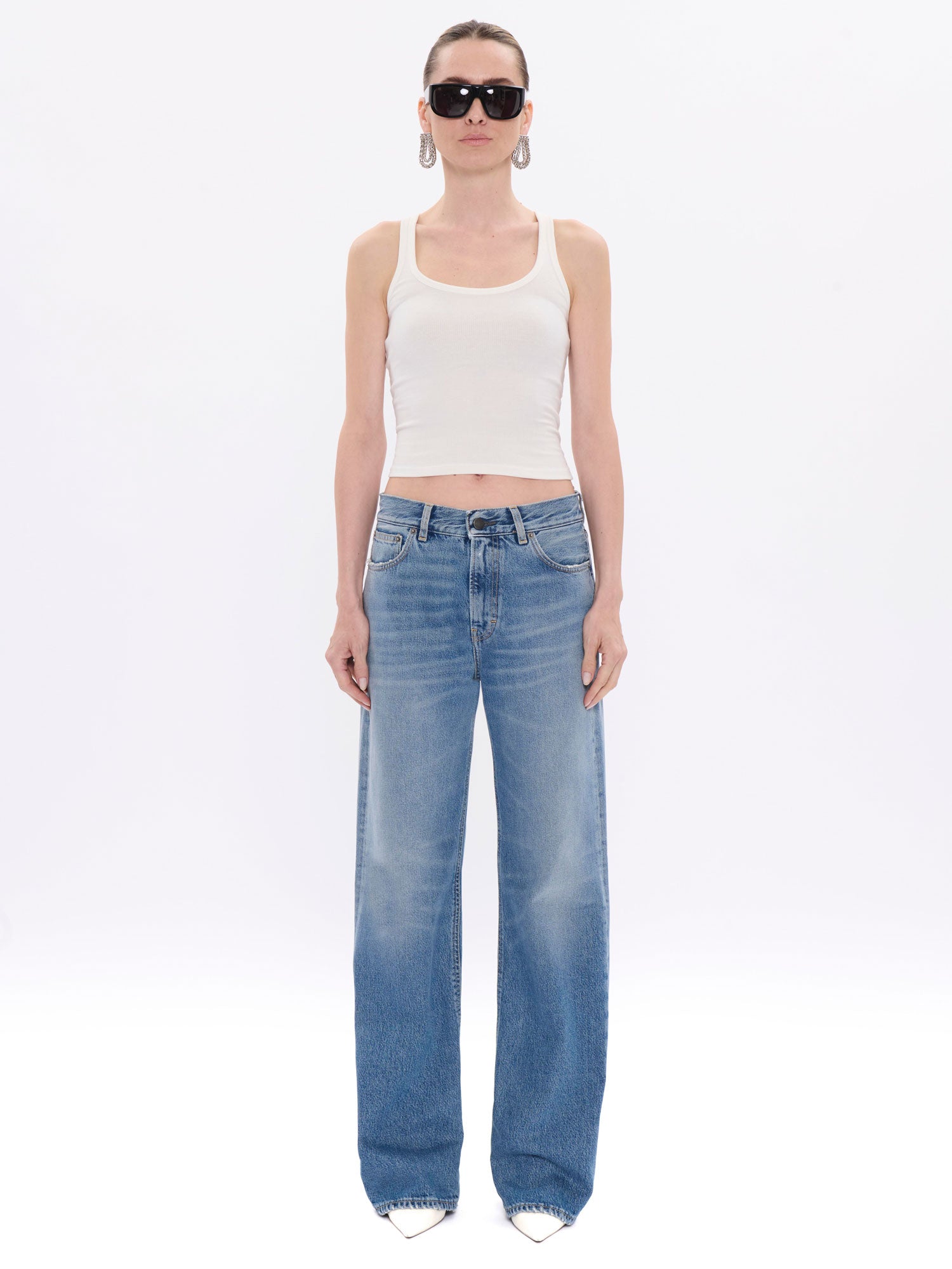 Woman wearing a white tank top and blue jeans on a white background