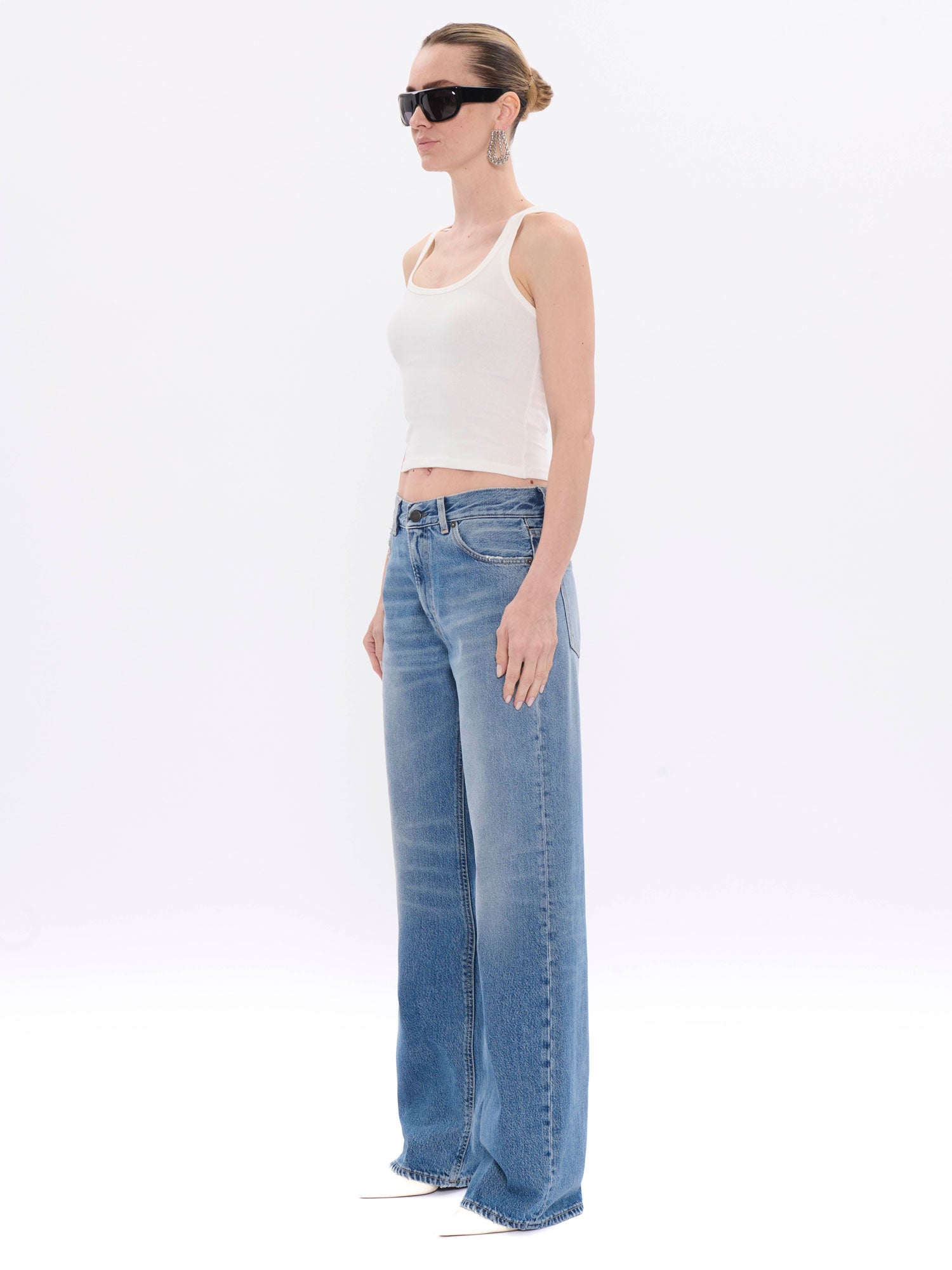 Woman wearing a white tank top and blue jeans on a white background