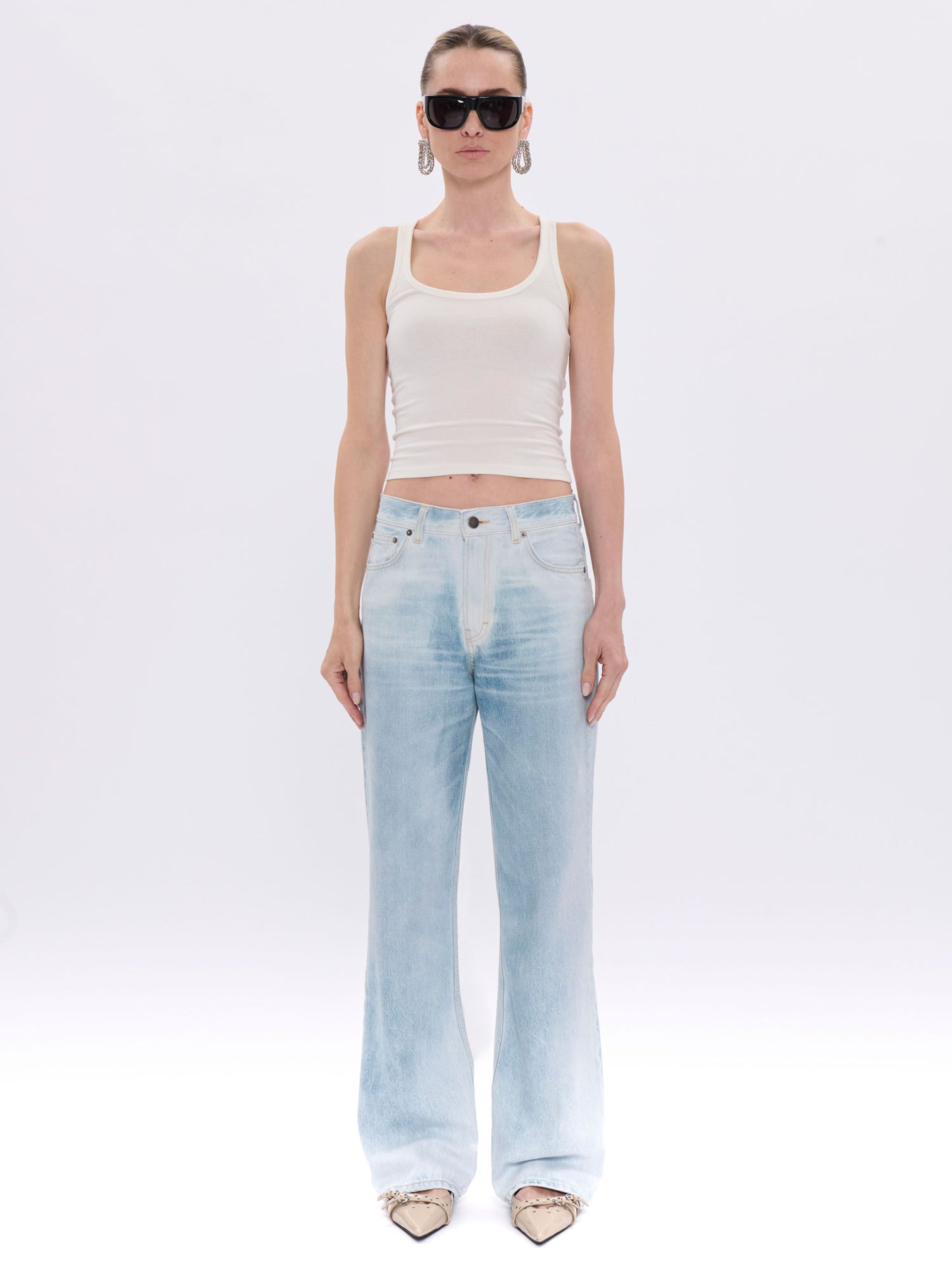 Woman wearing a white tank top and light blue jeans on a white background
