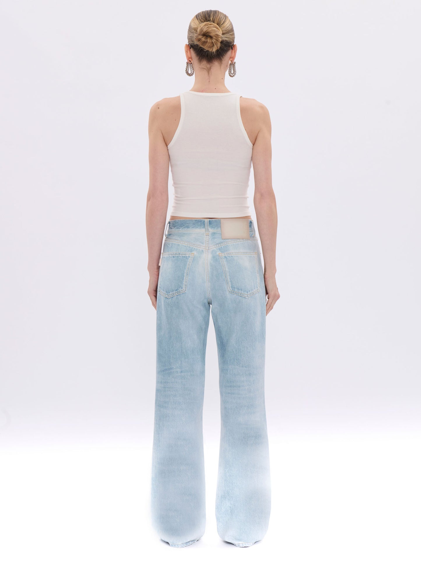 Person wearing light blue jeans and a white sleeveless top on a white background