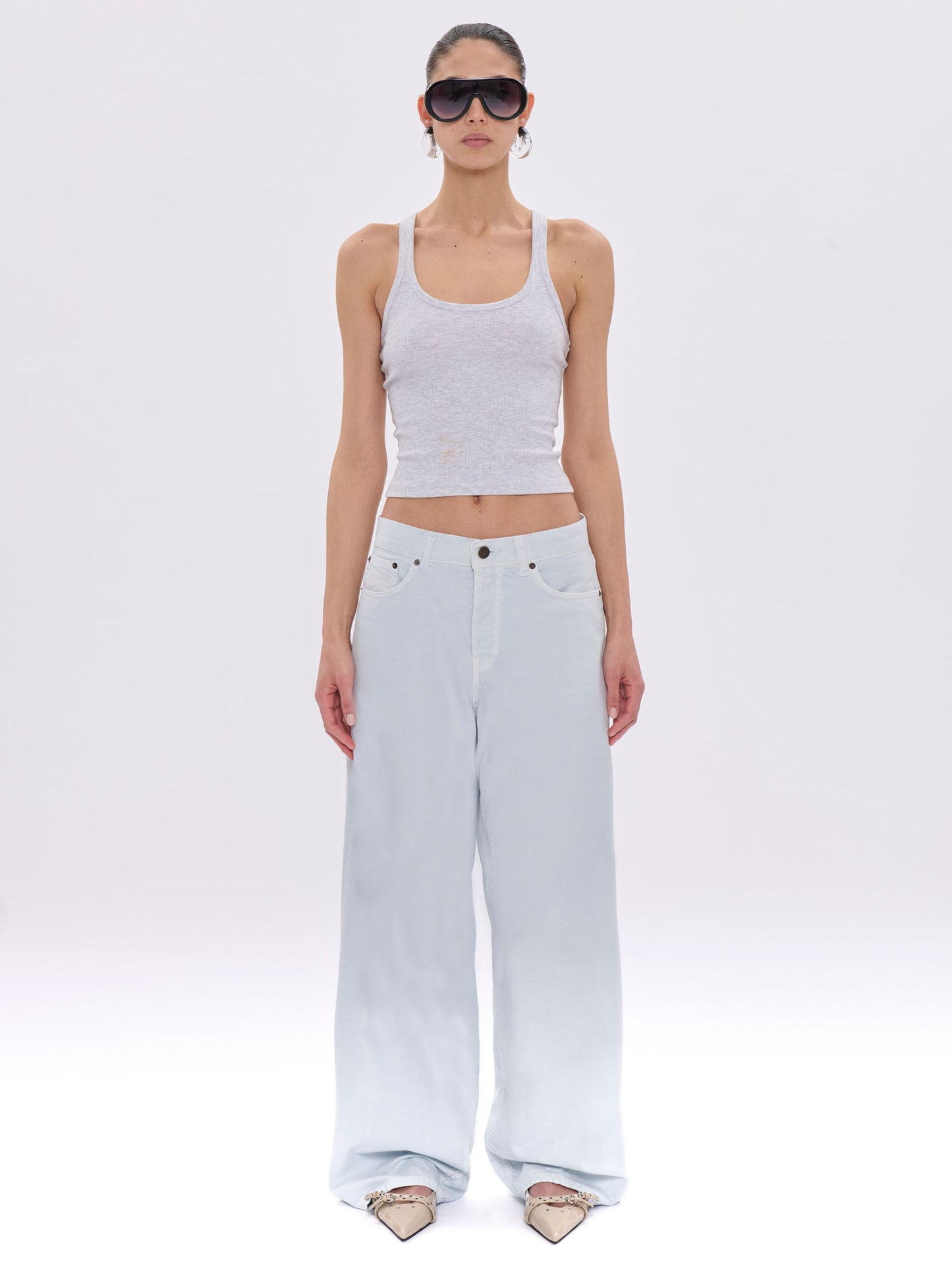 Woman wearing a white tank top and light blue jeans on a white background