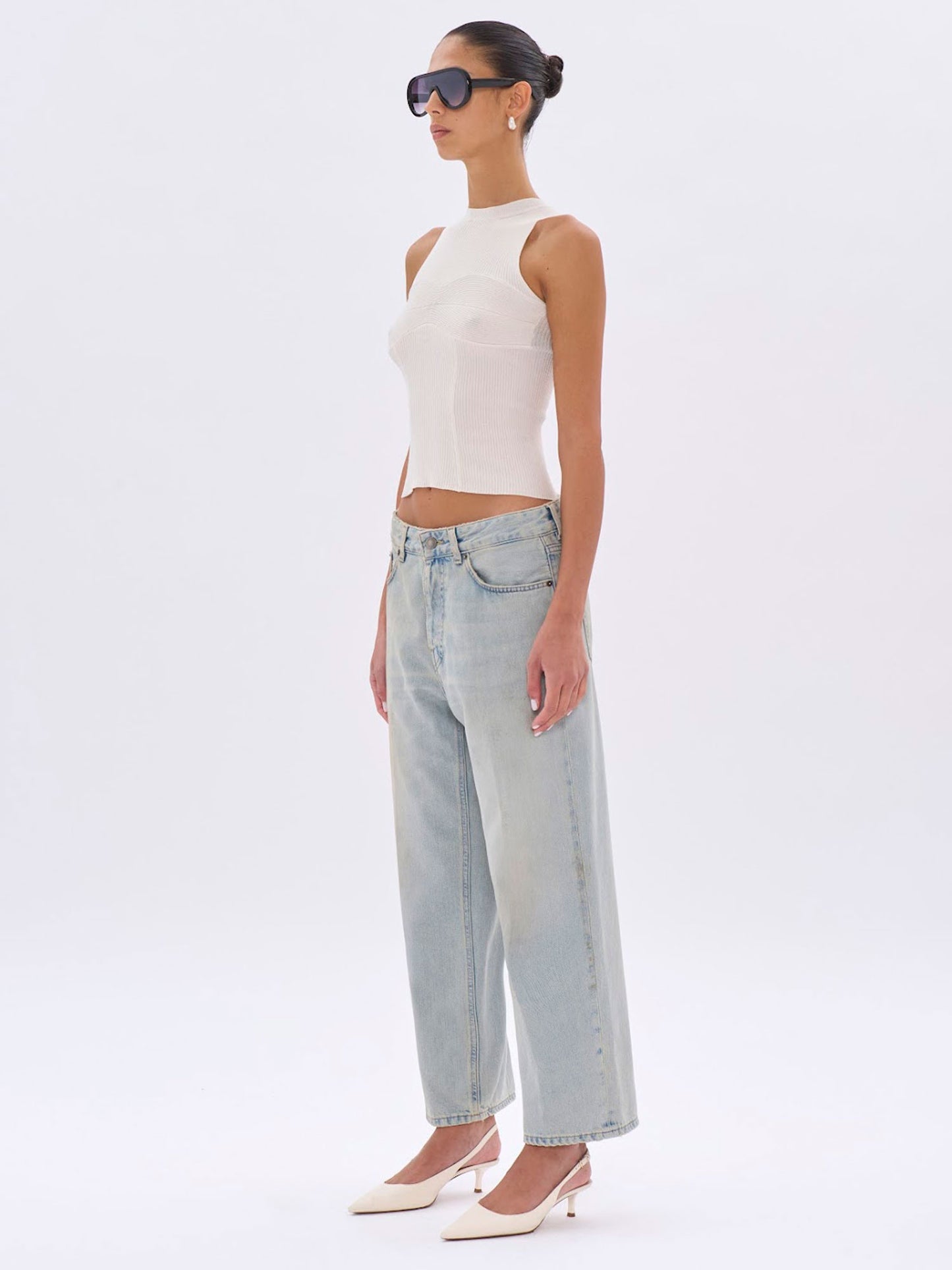 Woman wearing a white sleeveless top and light blue jeans on a white background