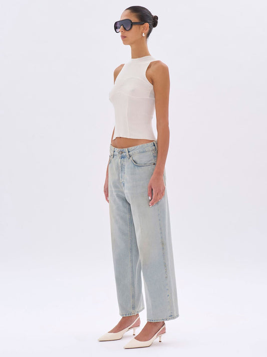 Woman wearing a white sleeveless top and light blue jeans on a white background